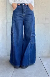 Pantalón tipo jean cargo de corte ancho y tiro alto, confeccionado en denim azul oscuro. Presenta bolsillos laterales tipo cargo con solapa y costuras reforzadas a lo largo de las piernas.