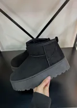 Botas cortas de gamuza sintética color negro, con interior forrado en piel sintética y suela de plataforma plana con relieve.