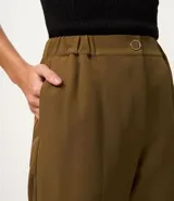 Pantalón femenino color verde oliva, confeccionado en crepé con modelo zanahoria, cintura alta y elástico para mayor comodidad. Posee cierre delantero con botón y bolsillos traseros.
