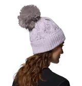 Gorro de lana tejido con diseño de ochos color lila, con vuelta y un pompón grande de piel sintética en la parte superior en tono tostado. Cuenta con una pequeña placa metálica con el logo de la marca en el borde.