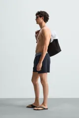 Bañador de hombre azul marino con cintura elástica gris y cordón ajustable. Presenta un pequeño texto estampado en relieve en la parte inferior izquierda.