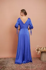 Vestido largo de satén color azul, con escote en V cruzado, mangas tres cuartos con detalles de lazos en los puños y falda larga con tajo frontal.