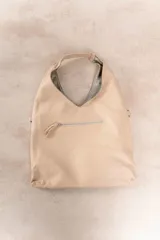 Bolso de hombro color beige, confeccionado en cuero sintético con interior plateado. Presenta un bolsillo externo con cierre.