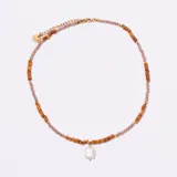 Gargantilla de cuentas facetadas en tonos rosados y ámbar/marrón, con un dije central de perla irregular de forma cuadrada. El cierre y la cadena de ajuste son dorados.