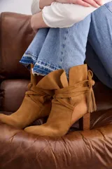 Bota de caña media en gamuzón color suela, con taco cuadrado y tiras envolventes en la caña terminadas en borlas decorativas.