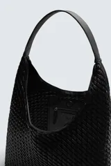 Bolso de hombro tipo hobo o shopper, color negro, con cuerpo de material trenzado. Posee un asa de hombro y un bolsillo interior con cierre de cremallera.