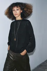 Camisa negra de manga larga con cuello redondo. Presenta detalles de entredós y jaretas verticales en el delantero, y cierre de botones en la espalda.