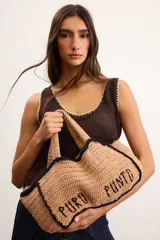 Bolso tipo tote mediano confeccionado en crochet artesanal color tostado, con detalles de bordes y costuras en contraste color negro. Presenta la inscripción "PURO PUNTO" bordada en el frente y asas dobles para llevar al hombro o en la mano.