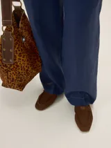 Cartera tipo bolso de cuero con estampado de cebra, asa de mano en cuero marrón y detalles de tachas metálicas.