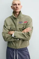 Cazadora cropped de algodón con efecto lavado, color verde militar. Presenta cuello solapa, cierre frontal con cremallera, bolsillos frontales de plastrón con solapa y parches decorativos en el pecho.