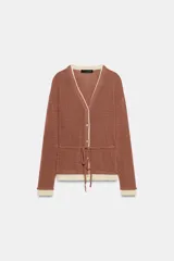 Chaqueta de punto color marrón con detalles en tono marfil en el escote en V, los puños y el ruedo. Cuenta con manga larga, cierre frontal con botones y un cinturón fino ajustable del mismo tejido.