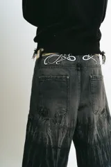 Bermuda de jean color negro con lavado acid wash gris. Presenta un corte baggy y detalles bordados en plateado y blanco que simulan ondas o llamas en la parte frontal superior e inferior.