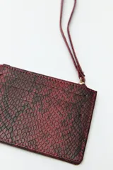 Billetera rectangular color bordó con estampado de piel de serpiente, cierre superior con cremallera, bolsillo frontal y correa de muñeca.