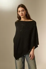 Poncho negro de tejido de punto con diseño asimétrico y detalle de pequeñas aplicaciones brillantes distribuidas por toda la superficie. Presenta un borde acanalado en el ruedo.