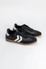 Zapatilla acordonada de estilo urbano, confeccionada en una combinación de materiales sintéticos en color negro, con detalles en blanco en los laterales y en el talón, y suela de goma color caramelo.