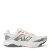 Championes New Balance Nitrel, diseñados para trail running y uso urbano, de color beige con detalles en gris y toques de naranja. Presentan capellada de malla transpirable con refuerzos, entresuela acolchada y suela con tracción especializada.