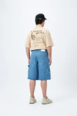 Bermuda de denim negro, estilo carpenter, con corte relajado y largo por encima de la rodilla. Presenta costuras visibles y múltiples bolsillos funcionales.