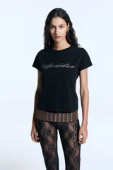 Remera de jersey de algodón con calce ajustado, escote redondo y manga corta. Presenta una estampa frontal con diseño de letras en glitter.