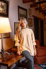 Blusa color beige de corte holgado, cuello alto con volados y mangas largas abullonadas con elástico en los puños.