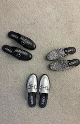 Suecos tipo mocasín de cuero metalizado plateado, con detalle de estribo metálico en el empeine y suela plana negra.