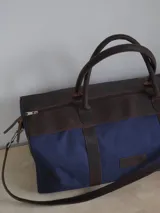 Bolso de lona color verde militar con detalles en cuero marrón. Tiene doble asa de mano y correa de hombro ajustable y extraíble.