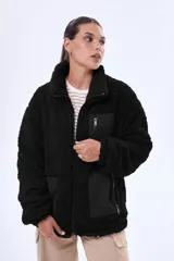 Campera de sherpa negra con cuello alto y cierre frontal completo. Presenta paneles de tela técnica en los bolsillos laterales y un bolsillo superior con cierre. Diseño de corte holgado y textura afelpada.