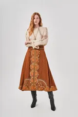 Falda larga marrón con estampado central de motivos florales en tonos naranjas y blancos, y pequeños puntos blancos distribuidos por toda la tela.