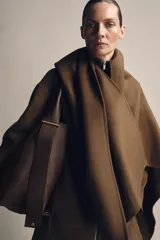 Bolso tipo saco de gran tamaño en cuero marrón oscuro, con textura granulada. Presenta un asa de hombro ancha y detalles metálicos dorados en la unión del asa. Incluye un bolsillo interior extraíble y cierre mediante botón imantado.