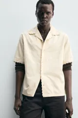 Camisa de corte relajado confeccionada en tejido de algodón, con cuello bowling y manga corta. Presenta un diseño con bordados geométricos a tono y cierre frontal de botones.