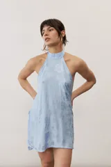 Top halter celeste con diseño asimétrico de corte más largo en la parte trasera, cuello alto y sutil estampado floral.