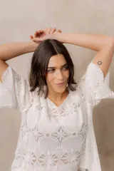 Blusa de punto calado color blanco, con diseño geométrico y floral transparente, escote redondo y mangas tres cuartos amplias de calce relajado.