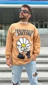 Buzo color beige con cuello redondo, puños y cintura acanalados. Estampado frontal con la frase "Peacefully Rolling" y un dibujo de una flor con una cara sonriente.