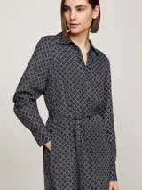 Vestido camisero midi azul marino con estampado geométrico en blanco, cuello camisero, manga larga con puños abotonados, cierre frontal con botones, cinturón de lazo y bajo asimétrico.