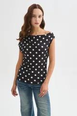Top de poliéster negro con estampado de lunares blancos, diseño al cuerpo y cuello asimétrico de manga corta.