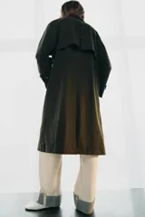 Trench oversize de color verde oscuro, con cuello de piel en tono marrón a contraste. Presenta manga larga con trabillas en los puños, bolsillos delanteros, cierre frontal con cremallera y botones ocultos bajo solapa, y abertura en la espalda.