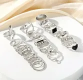 Set de 27 anillos plateados con diferentes diseños: lisos, con forma de serpiente, con corazones, con piedras negras, con forma de mariposa y con eslabones.