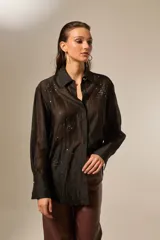 Camisa negra de lyocell, manga larga, con cuello camisero y botones frontales. La prenda está adornada con pequeños apliques de strass distribuidos por toda la tela.