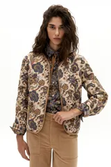 Chaqueta reversible con un lado de twill de lana a cuadros en tonos beige, marrón y gris, con vivos en pana color camel y bolsillos frontales. El otro lado es de algodón capitoneado con estampado de arabescos. Tiene cuello a la base y botones metálicos a presión escondidos.