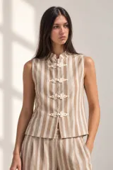 Chaleco a rayas verticales en tonos beige y blanco, sin mangas, con cuello mao y cierre frontal con nudos chinos decorativos.