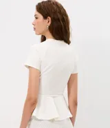 Blusa de punto Roma color celeste, con cuello alto, mangas cortas y diseño peplum. Presenta recortes estructurales y un cinturón integrado con hebilla metálica en la cintura, finalizando en un ruedo con volados.