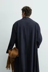 Trench de corte relajado confeccionado en tejido con viscosa, de color azul marino. Presenta cuello con solapas de muesca, cierre frontal de botonadura cruzada, mangas largas con puños ajustables mediante trabillas y bolsillos de vivo en la cadera. Incluye una abertura central en la espalda.