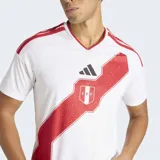 Camiseta de fútbol Adidas de la Selección Peruana, modelo Primera Equipación 26. Diseño principal blanco con una franja diagonal roja con textura geométrica que cruza el pecho, donde se ubica el escudo de la FPF. Presenta cuello en V y tres franjas rojas en los hombros.