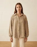 Camisa de calce amplio color verde oliva, con cuello camisero, hombros caídos y mangas largas con puños elásticos. Presenta detalle de frunce en el delantero y espalda, con cierre frontal de botones.