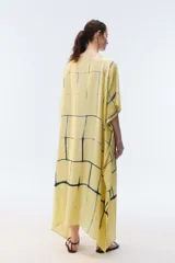 Kaftan maxi amplio de color amarillo, con escote redondo, mangas cortas y ruedo irregular. Presenta un diseño estampado a cuadros con efecto teñido.