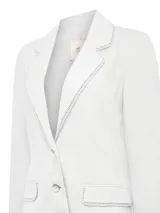 Blazer de lino orgánico color blanco, con cuello sastre, cierre frontal de dos botones y dos bolsillos con solapa. Presenta un delicado detalle de calado artesanal en los bordes del cuello y las solapas de los bolsillos.