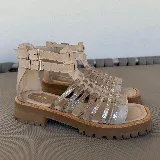 Sandalias bajas de cuero color beige con tiras horizontales plateadas y cierre con hebilla al tobillo.