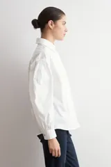 Camisa de corte oversized, color blanco, con cuello clásico, cierre frontal de botones y mangas largas.
