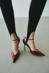 Zapato de tacón alto y fino con acabado en punta, escote en pico y cierre mediante hebilla en la pulsera del tobillo, en color bordó con acabado charol.