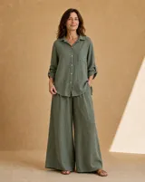 Camisa de lino color verde seco, de corte holgado, con cuello camisero, cierre frontal de botones de nácar, bolsillo aplicado en el pecho y mangas largas con tirilla para sujetar remangadas.