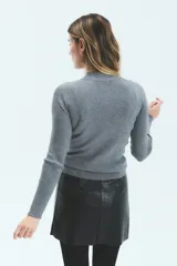 Polera de tejido de punto acanalado, color gris, con cuello alto y mangas largas. Presenta un ajuste al cuerpo y largo hasta la segunda cadera.